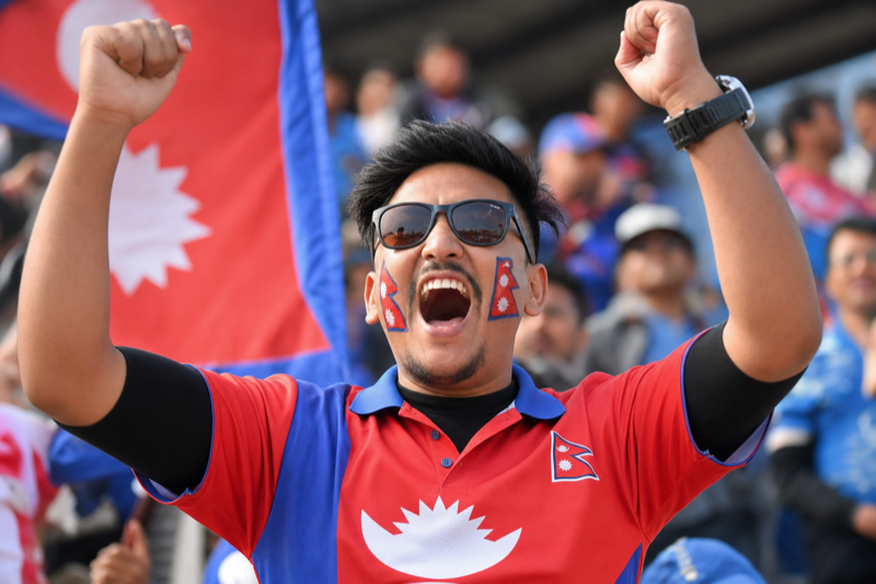 Cricket fan in the stands at a Nepal match — shouting and cheering with the Nepali flag