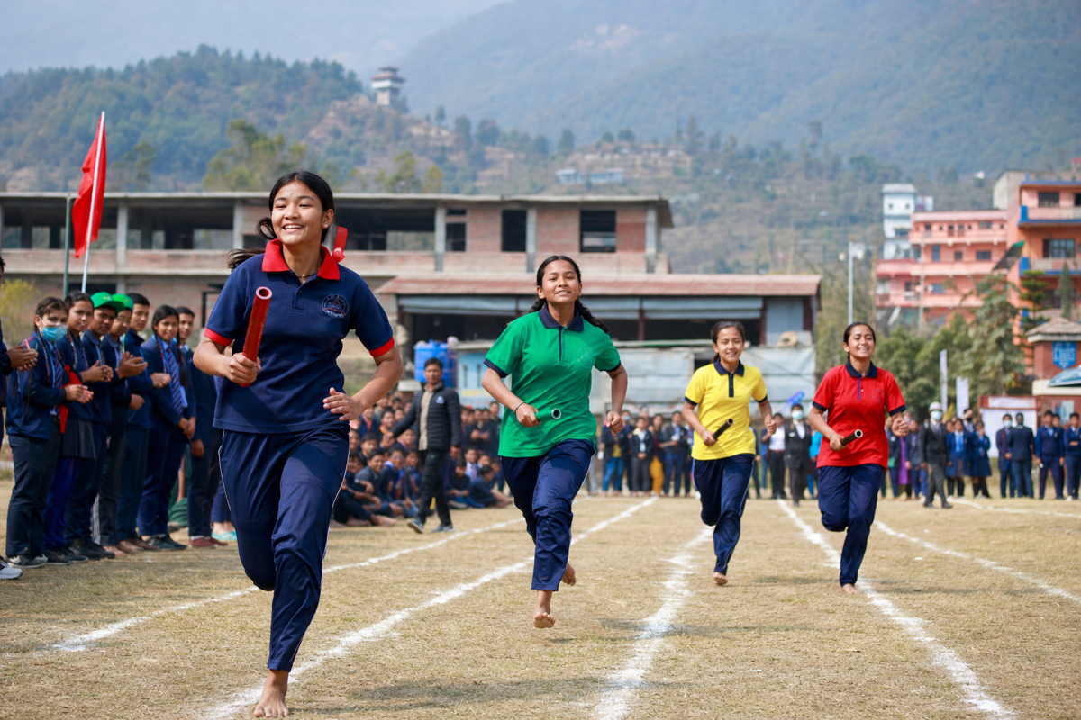 Nepali school students competing at an outdoor sports day — runners in uniform on the athletics field with smiling faces